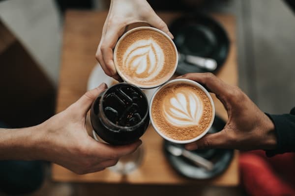Latte art being poured — a rosetta forming in a ceramic cup on a wooden counter